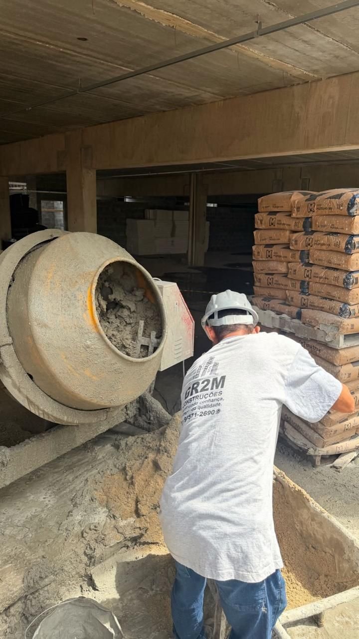 Profissional com uniforme GR2M preparando massa ao lado de betoneira